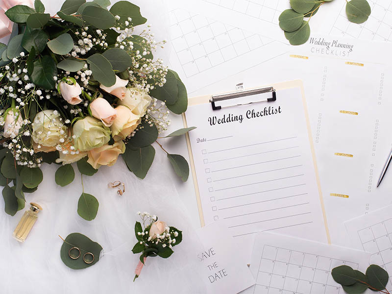 A wedding checklist along with save the date cards a calendar and bouquet of roses.